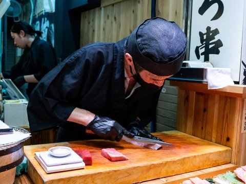 Japanese chef meticulously slices fresh tuna for sushi.