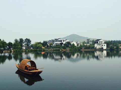 brown wooden boat on body of water overlooking houses by the shore at daytime