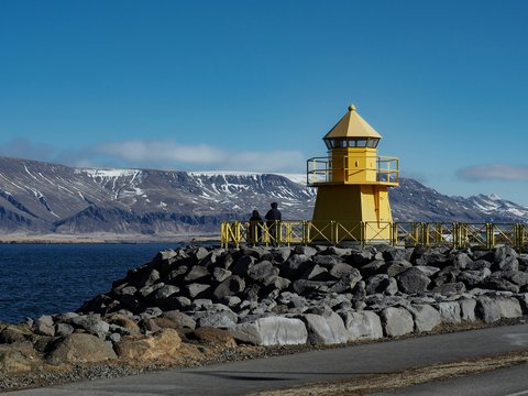 a yellow lighthouse sitting on top of a rocky shore