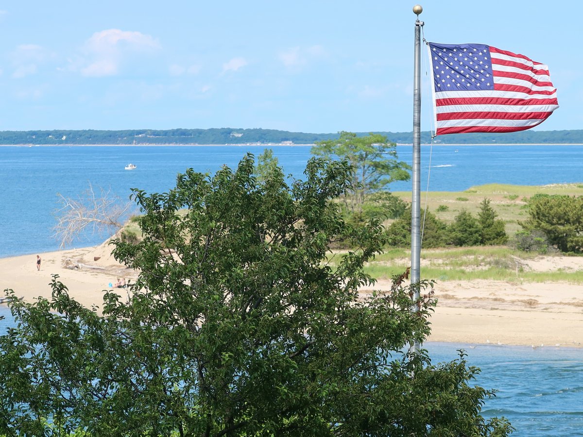 a large american flag flying over a beach next to a body of water