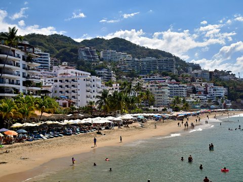Beach with umbrellas and people, city on hill