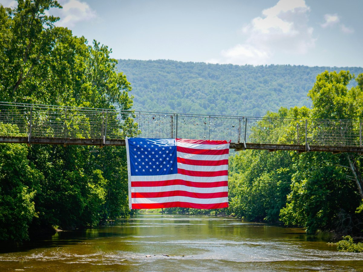 An american flag hangs from a bridge over a river.