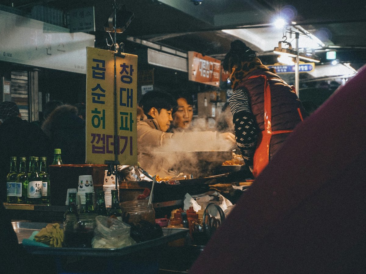 man in red and black jacket standing in front of food stall