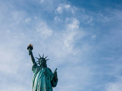 low angle photo of Statue of Liberty under blue and white cloudy daytime sky
