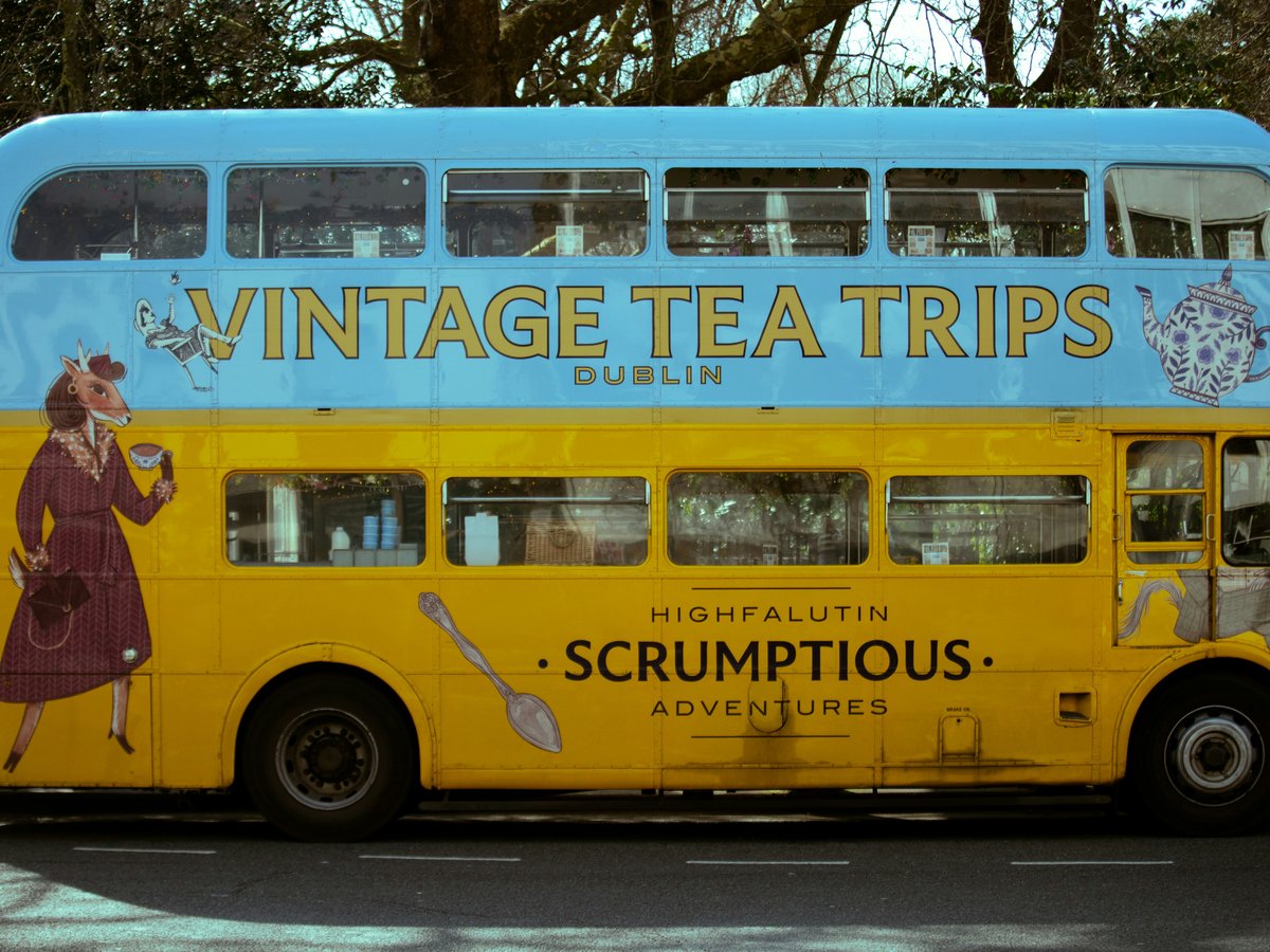 A yellow and blue double-decker bus with "vintage tea trips"