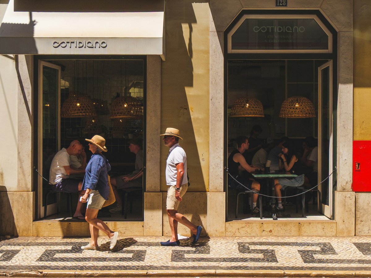 People walk past a cafe on a sunny day.