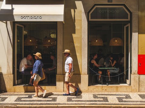 People walk past a cafe on a sunny day.