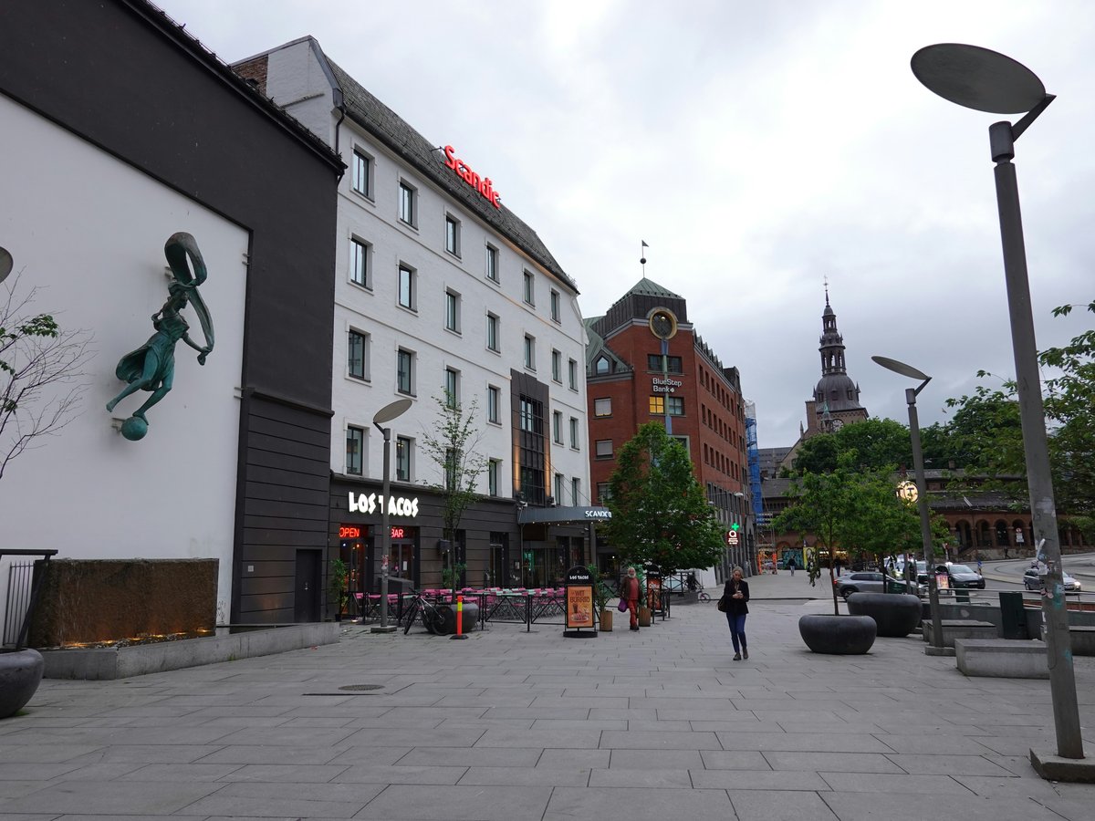 City square with modern buildings and a distant church spire.