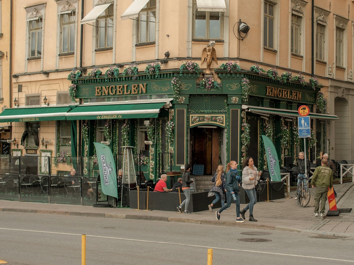 People walk past a green restaurant on a city street.