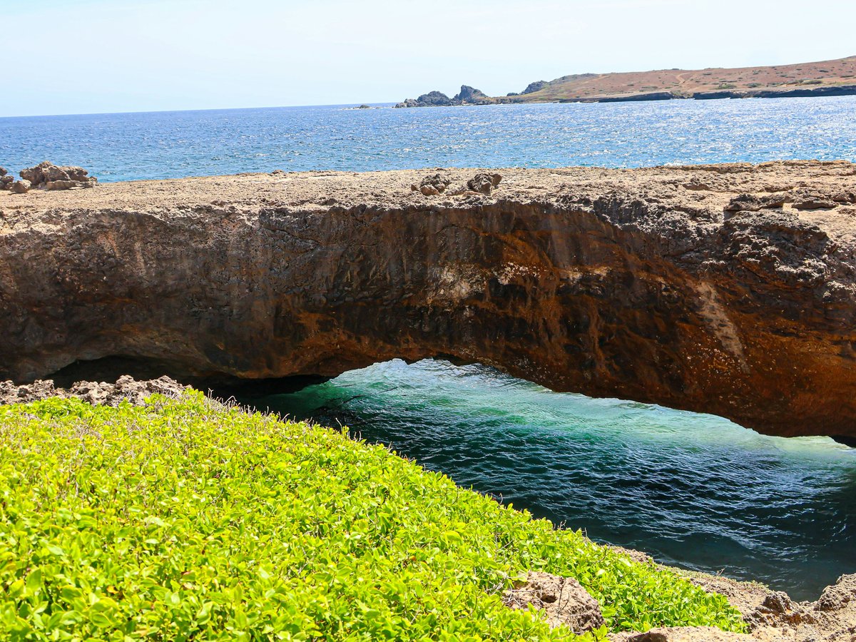 Natural rock arch over clear turquoise ocean water.