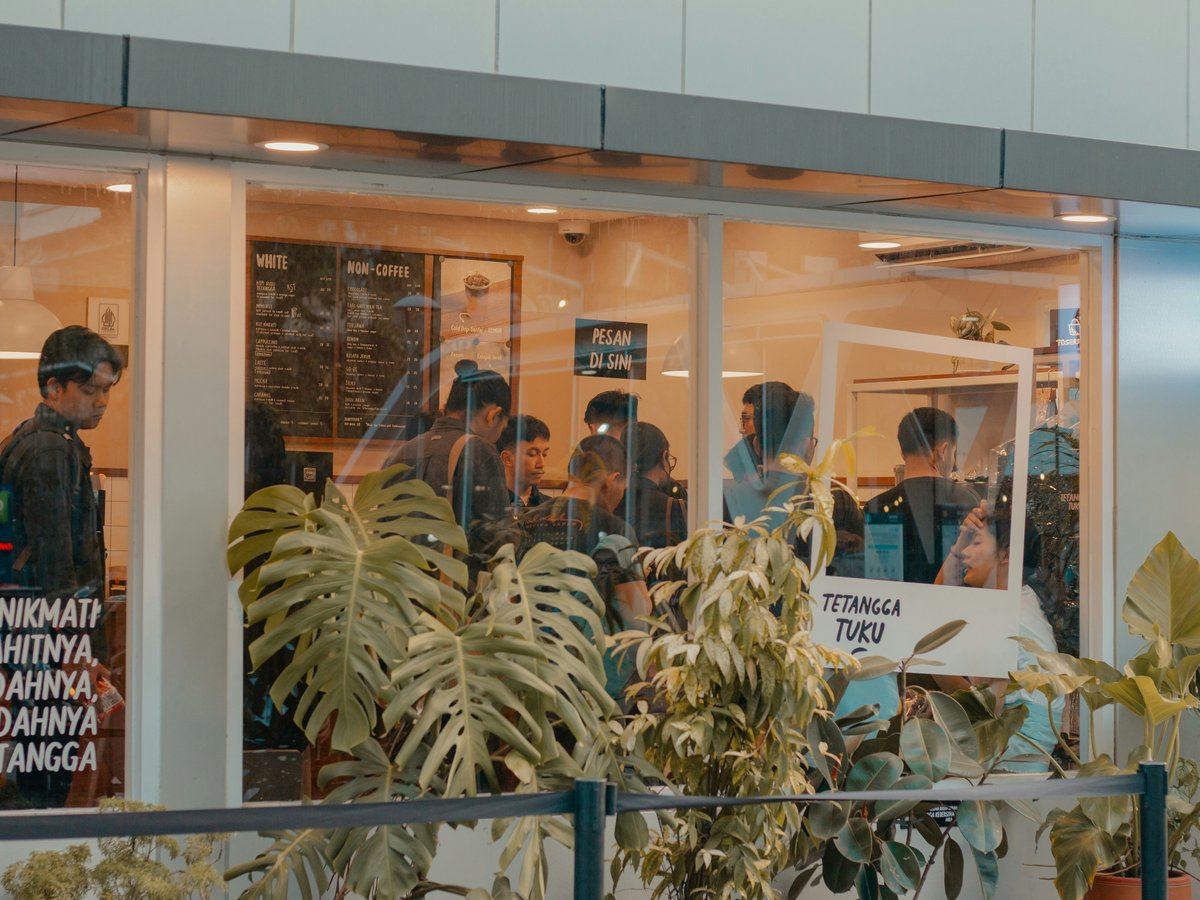 People queue inside a coffee shop with plants