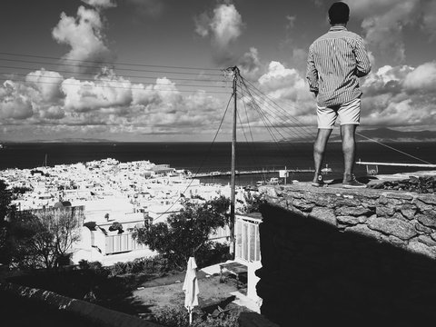 man in white long sleeve shirt and white pants standing on rock near body of water