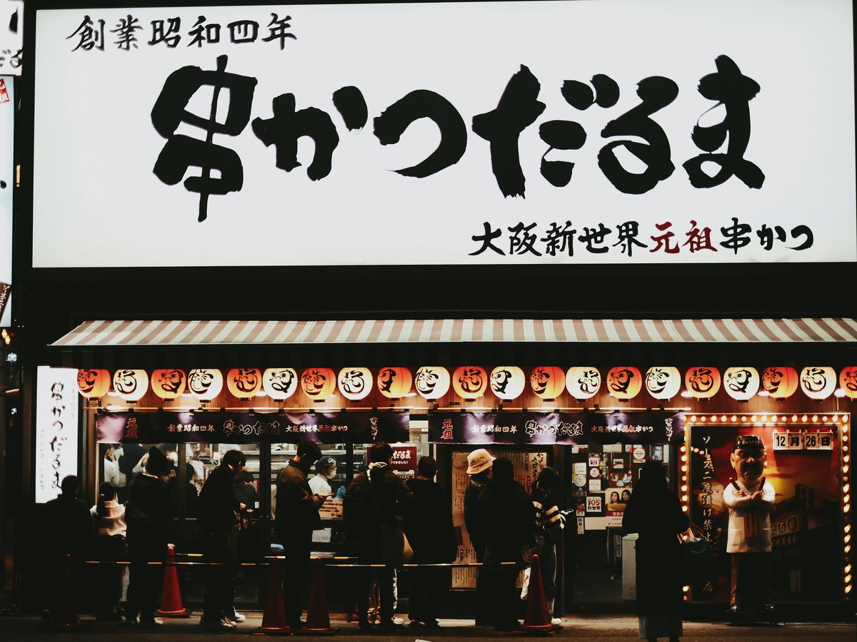 People queuing outside a japanese restaurant at night.
