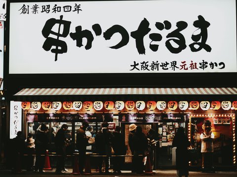 People queuing outside a japanese restaurant at night.