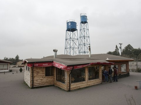 People near a wooden building and two tall water towers