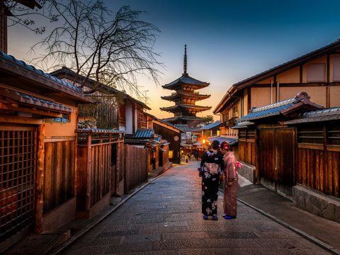 two women in purple and pink kimono standing on street