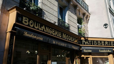 A corner Parisian boulangerie with gilded 'Boulangerie Moderne' lettering, warm storefront windows stacked beneath classic Haussmann balconies