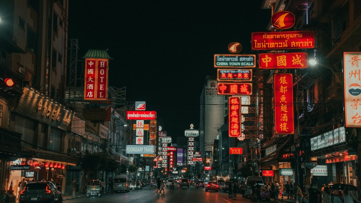 Yaowarat at night, the red Chinese neon signs of Bangkok's Chinatown glowing above a slow-moving crowd of pedestrians and cars