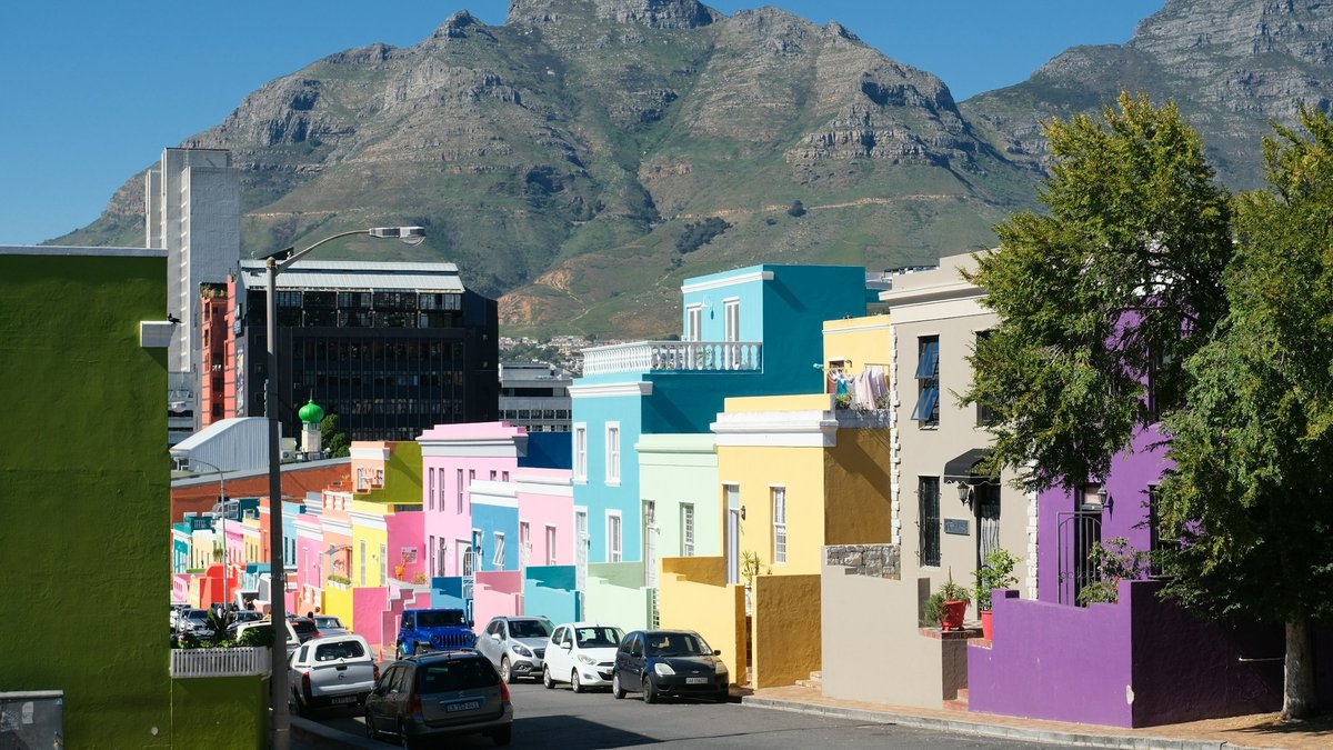 A row of pastel Bo-Kaap houses in green, pink, blue, yellow and purple lines a sloping street, the rocky face of Devil's Peak rising above the rooftops