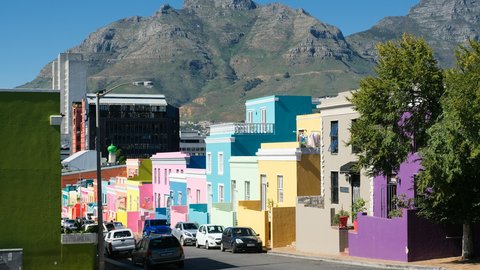A row of pastel Bo-Kaap houses in green, pink, blue, yellow and purple lines a sloping street, the rocky face of Devil's Peak rising above the rooftops