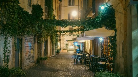 A hushed Trastevere lane after dark, cobblestones slick under warm lamplight as empty trattoria tables and ivy-draped walls recede into a soft amber glow