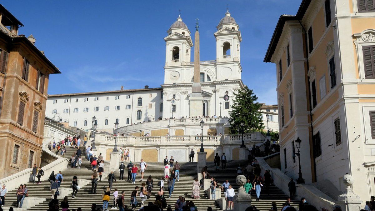 Late-afternoon crowds linger on the Spanish Steps, pastel palazzi framing the scene as locals and travellers sprawl across the travertine to trade gelato and conversation