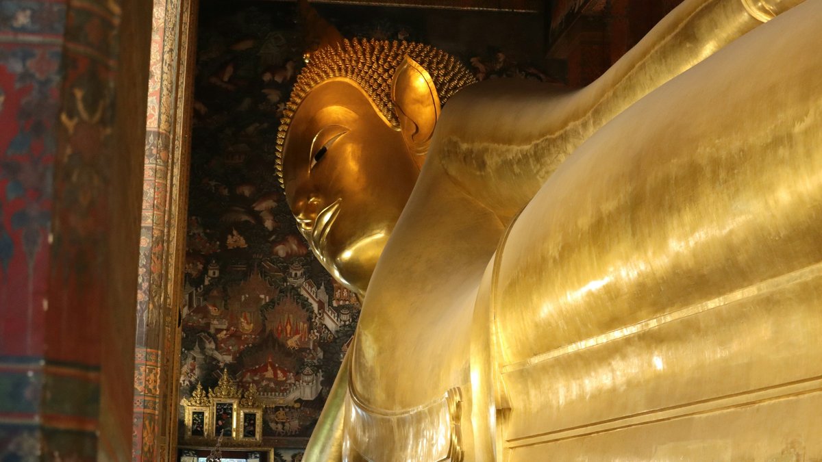 The reclining Buddha at Wat Pho, gold leaf glowing against the temple's intricately painted murals in soft interior light