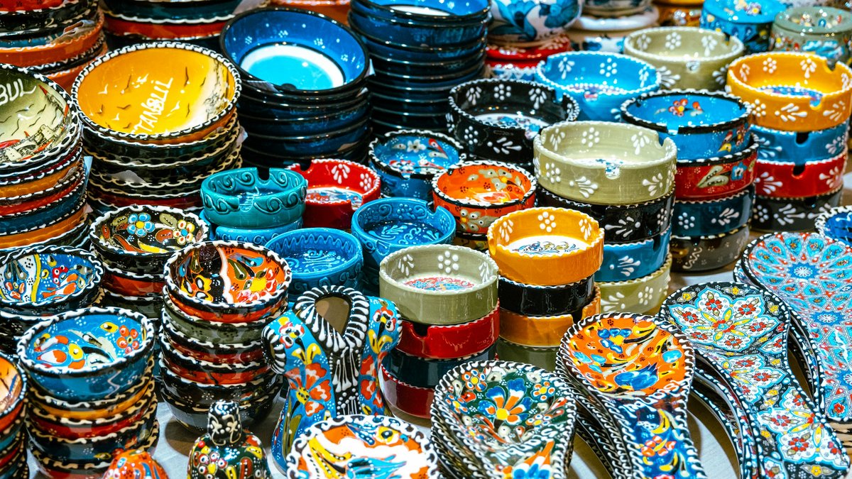 A Grand Bazaar stall stacked with hand-painted Turkish ceramic bowls in cobalt, turquoise, scarlet, and saffron, each one crowded with floral Iznik patterns