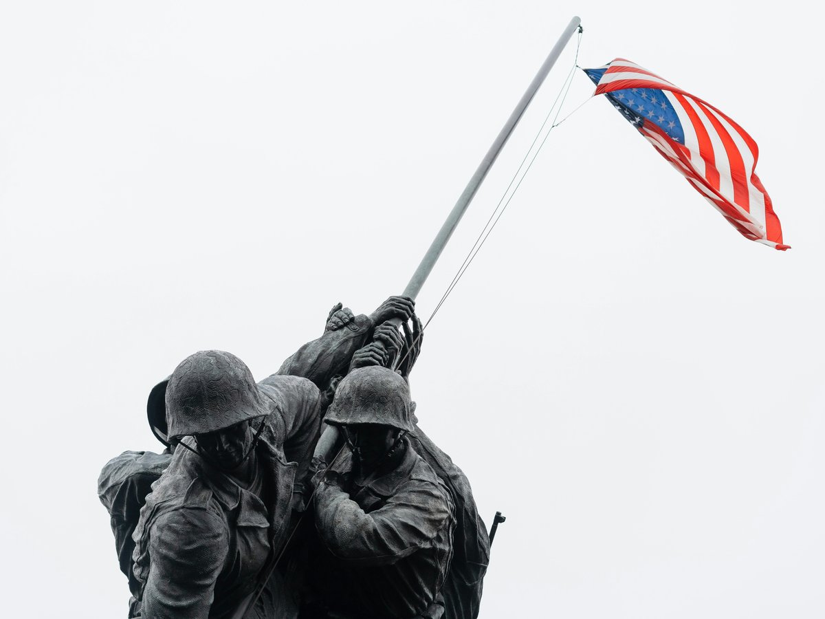 A couple of soldiers holding a flag on top of a hill