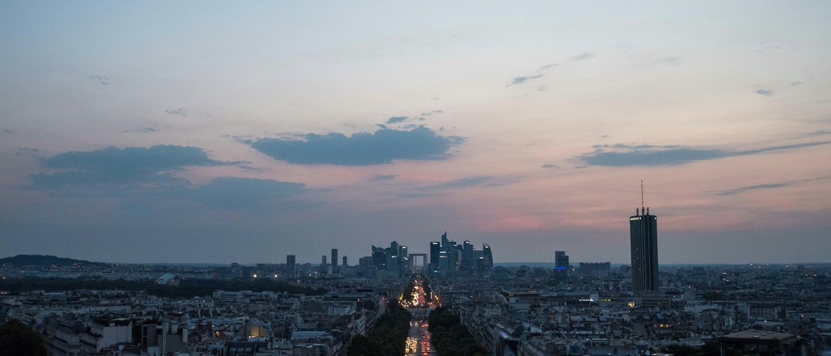 The Champs-Élysées stretching from the Arc de Triomphe toward La Défense at blue hour, rooftops glowing under a pink-streaked Paris sky