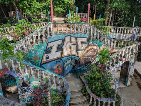 Ornate concrete stairs covered in graffiti and overgrown plants.