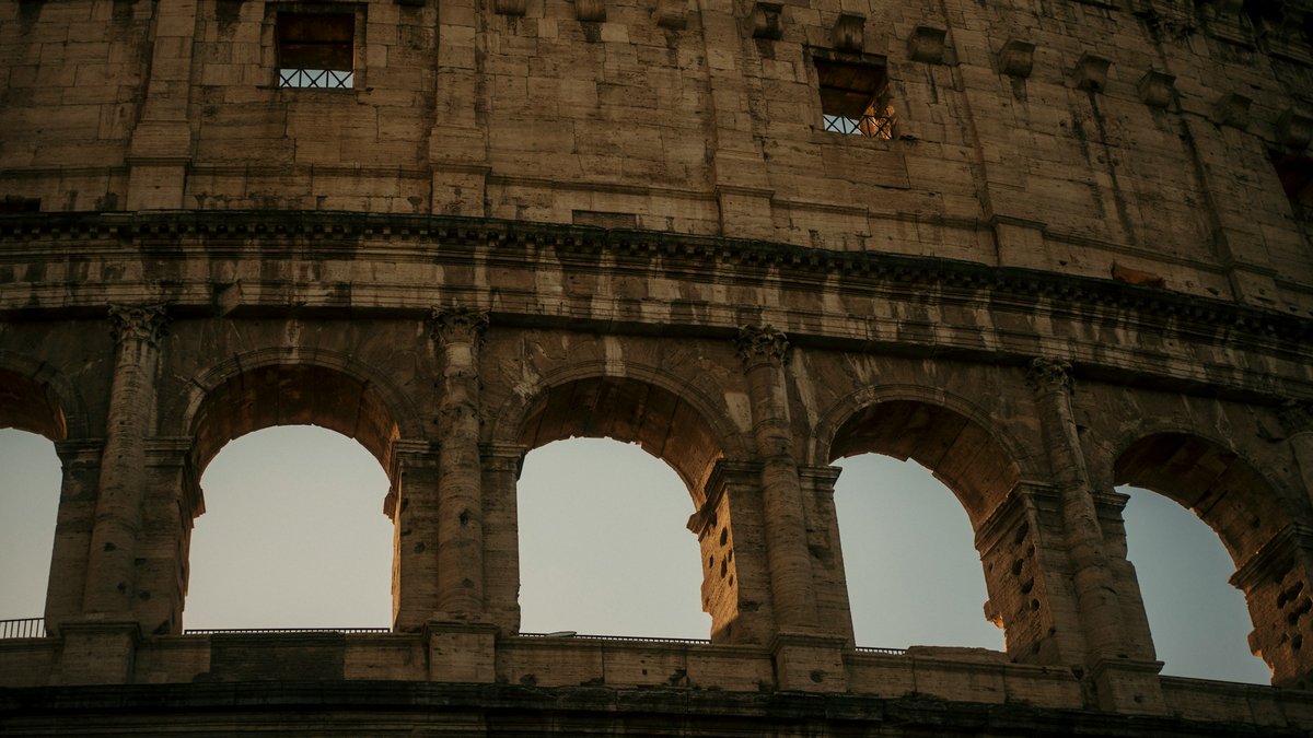 A close-up of the Colosseum's tiered stone arches catching the last burnt-orange light of sunset, each ancient curve rimmed in gold as the sky above melts to indigo
