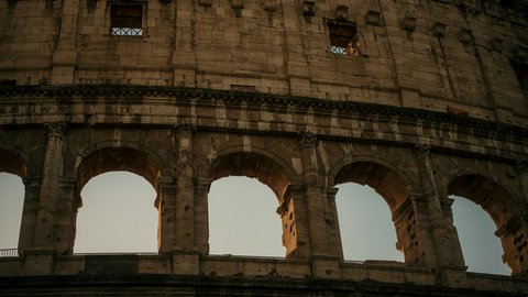 A close-up of the Colosseum's tiered stone arches catching the last burnt-orange light of sunset, each ancient curve rimmed in gold as the sky above melts to indigo