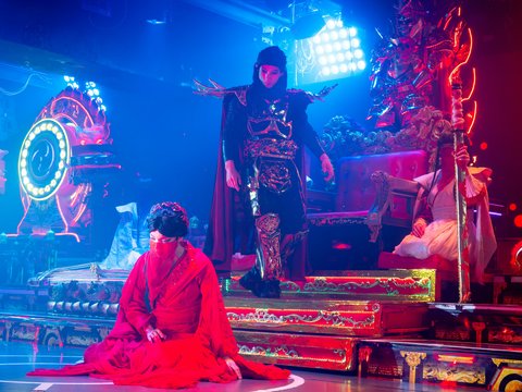 A person in ornate black armor walking down steps near a person in red