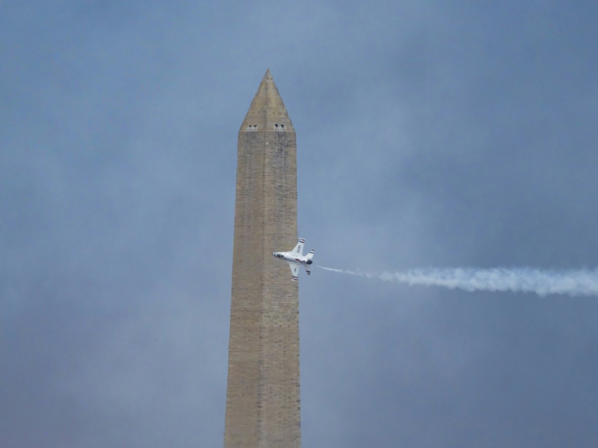 A jet flies past the washington monument, leaving a contrail.