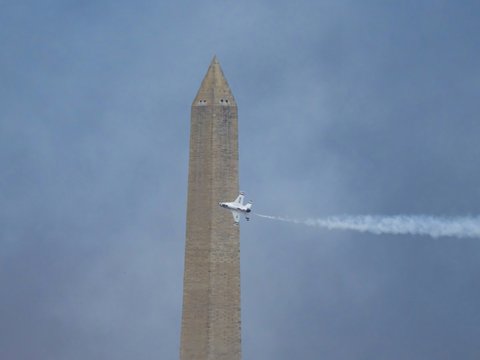 A jet flies past the washington monument, leaving a contrail.