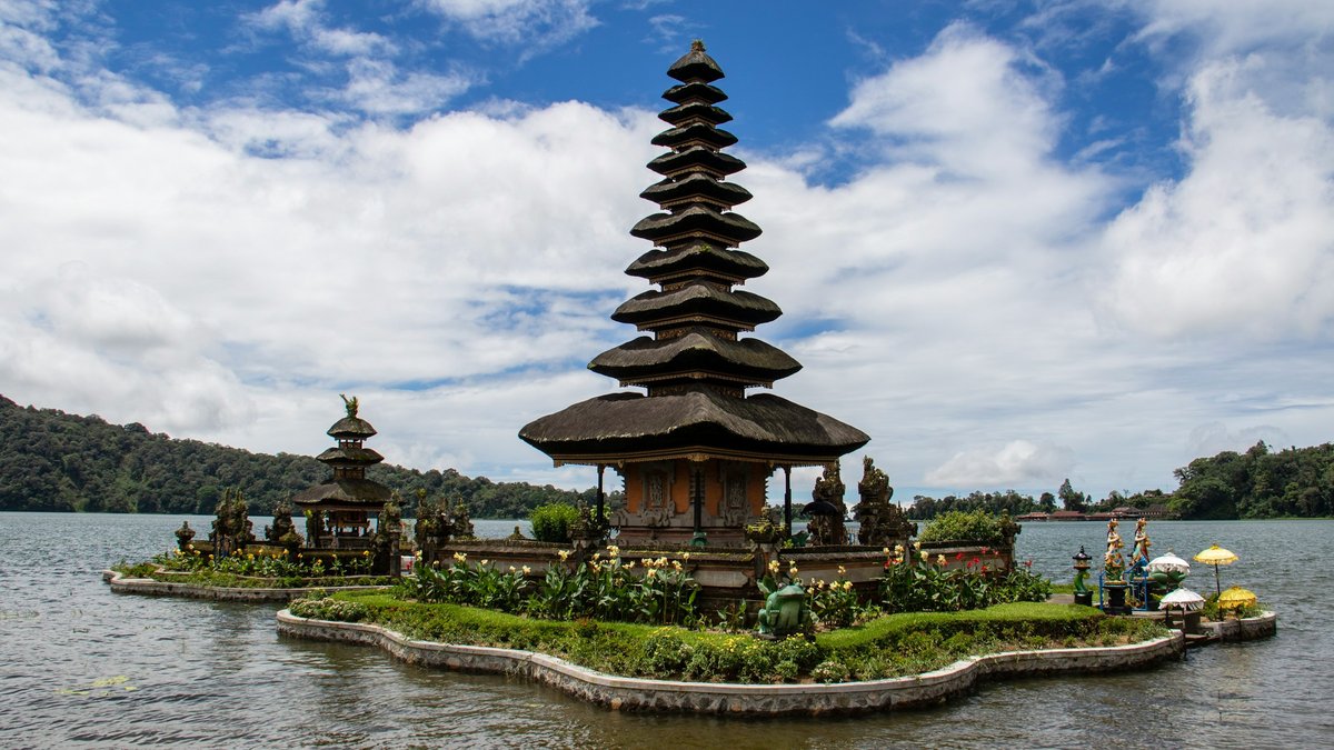 The tiered black-thatched meru of Pura Ulun Danu Beratan rises from Lake Bratan's still water, garlanded by ceremonial umbrellas, offering stupas and jungle-dark caldera ridges beyond