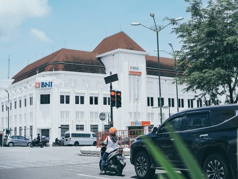 a man riding a motorcycle down a street next to a tall white building