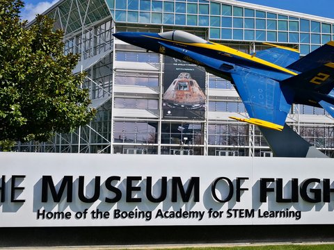a blue and yellow fighter jet flying over a museum of flight sign