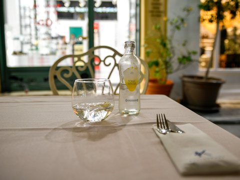 Outdoor cafe table with a glass, bottle, and cutlery.