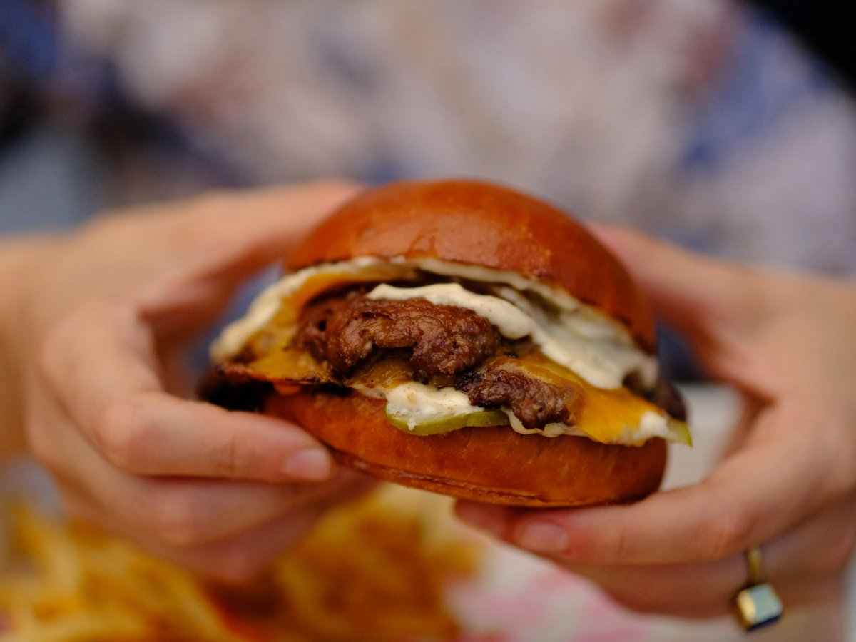 Person holding a juicy cheeseburger with fries