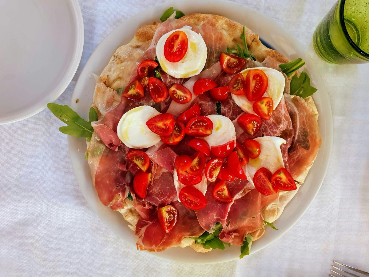 pizza with sliced tomato and green leaf vegetable on white ceramic plate