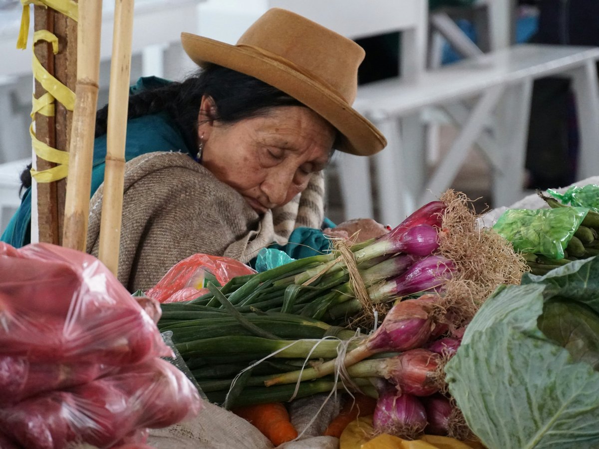 An old woman sitting at a table filled with vegetables