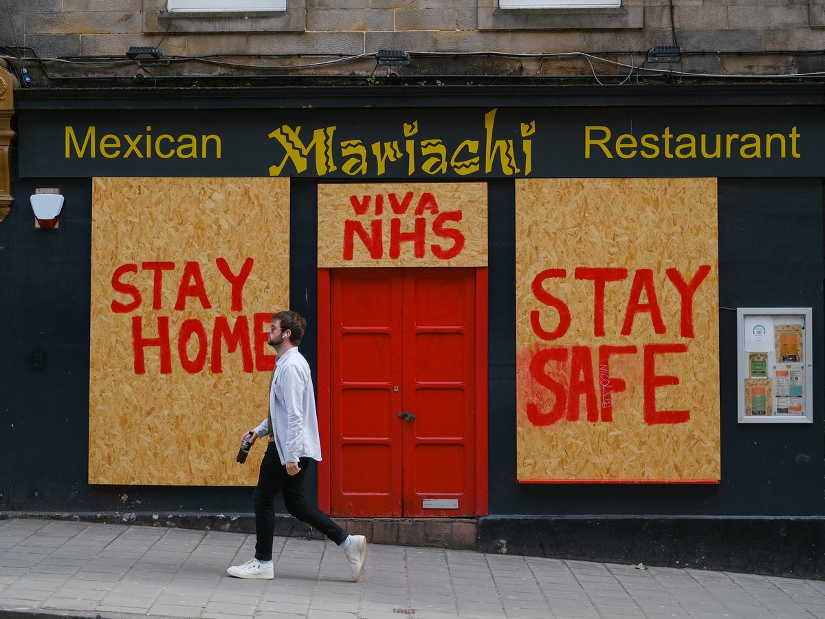 a man walking past a mexican restaurant with boarded up doors
