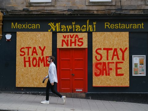 a man walking past a mexican restaurant with boarded up doors