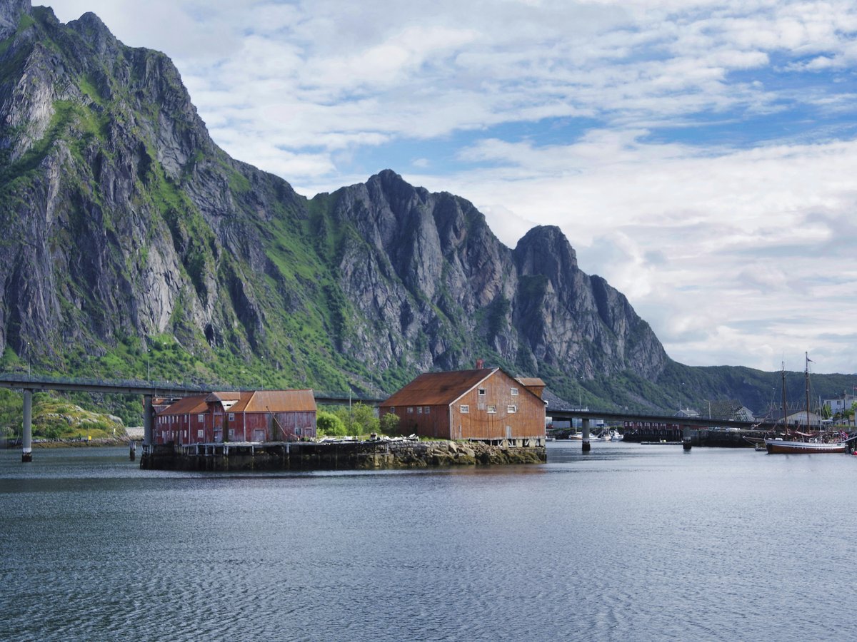 brown wooden house near body of water and mountain under cloudy sky during daytime