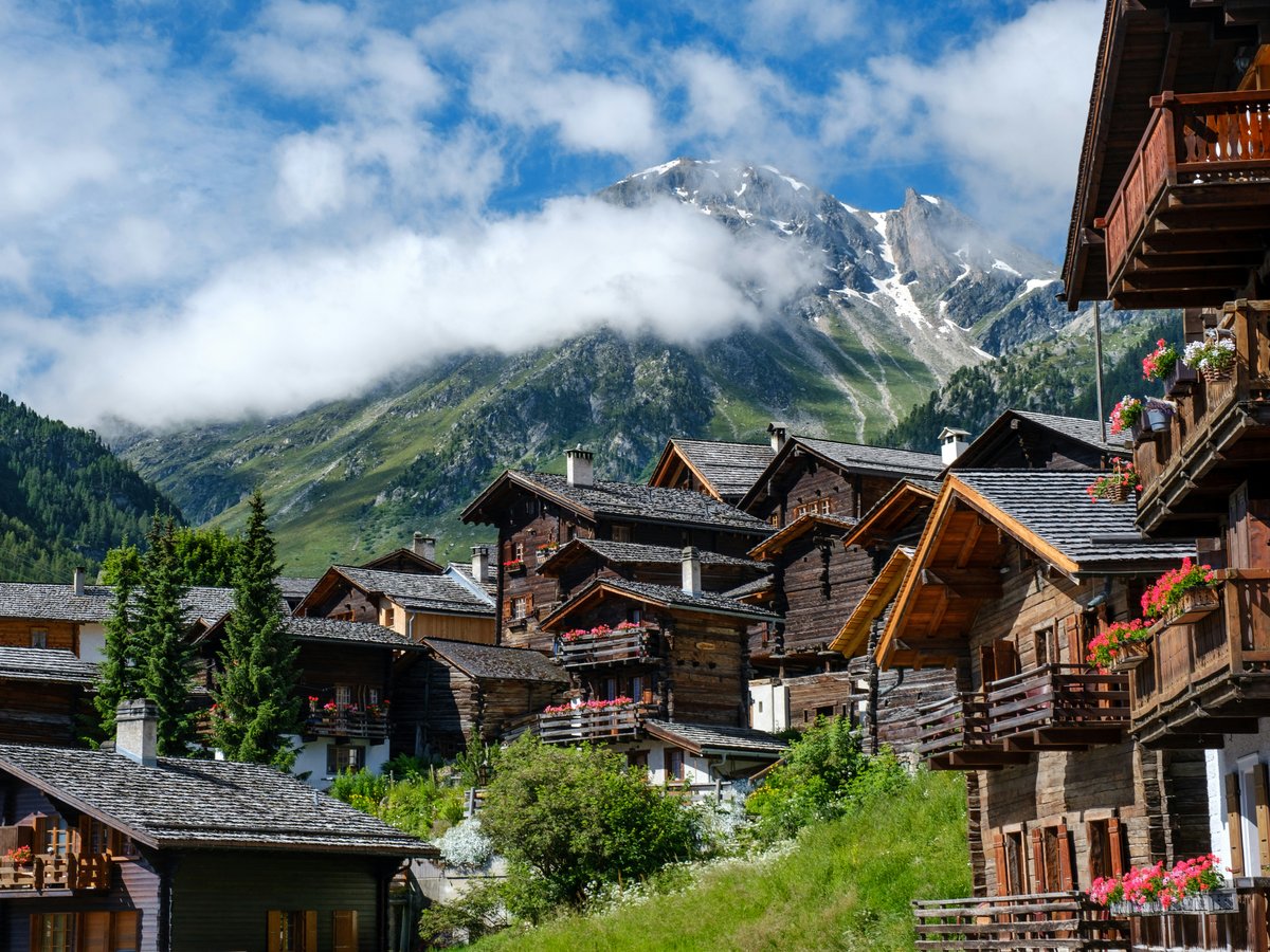 brown wooden houses near green trees and mountain under white clouds during daytime