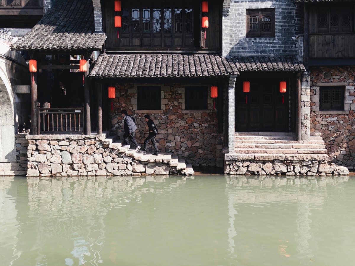 A man riding a bike past a building next to a body of water