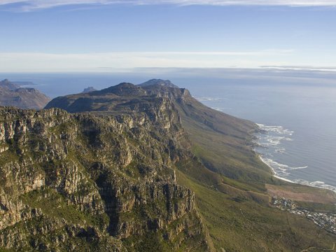 Mountains stand next to the ocean under a blue sky.