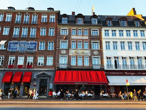 People dining outside buildings with red awnings